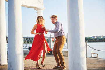 Happy beautiful woman in red dress and young man dance of on summer with lake in the background. Color contrast red and white