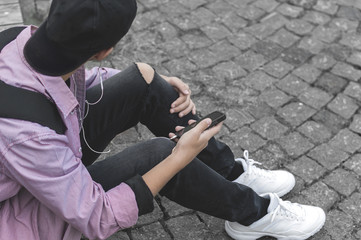 young man with phone sitting on the sidewalk