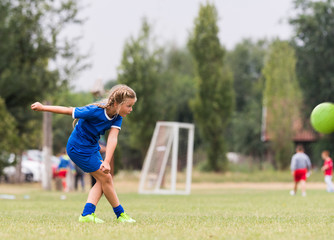 Naklejka premium Kids soccer football - little girl is shooting ball at soccer field