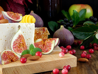 Cheese made of sheep milk and slices of figs on a wooden board surrounded by cranberries and almond. Ingredients for a cheese plate