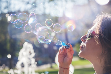 beautiful young woman blowing soap bubbles in the sun