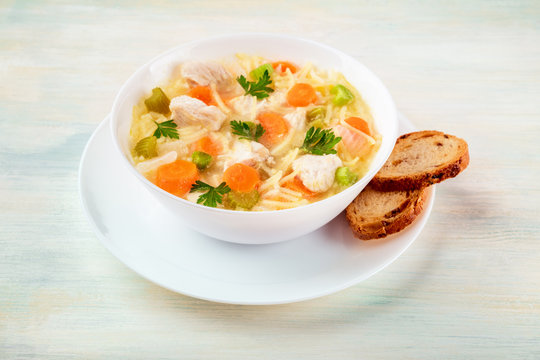 Chicken soup with noodles and bread on a light background