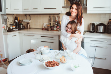 Fototapeta na wymiar mother having breakfast with teen daughter at home in modern white kitchen. Casual lifestyle in real life interior