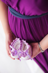 Happy pregnant woman heart symbol love touching tummy holding baby shoes