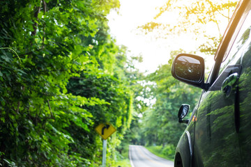 Rear view mirror of gray color car on outback road in the morning time with sunlight and blurred green forest in the background