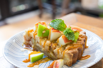 Apple pie with fresh green and red apple and mint on top in ceramic plate on wooden table