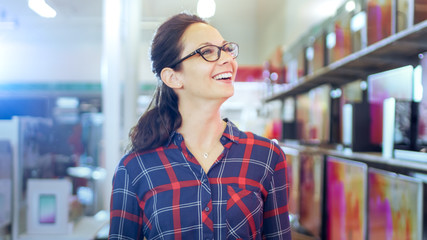 Beautiful Young Woman Walks In the Electronics Store Browsing Shelves with Latest Models of 4K UHD TV's. She Smiles in that Big, Bright Modern Store that Has all the New Devices.