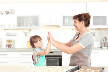 Fototapeta premium Cute little girl and her grandmother making cookies on kitchen