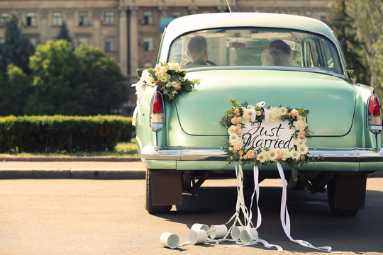 Wedding couple in car decorated with plate JUST MARRIED and cans outdoors