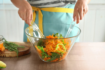 Woman making carrot salad in kitchen
