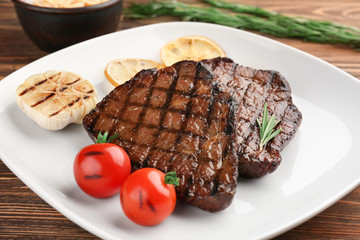 Plate with delicious grilled steaks on wooden table