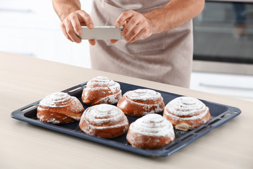 Young blogger taking photo of tasty pastry in kitchen
