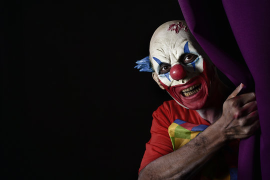 scary evil clown peering out from a stage curtain