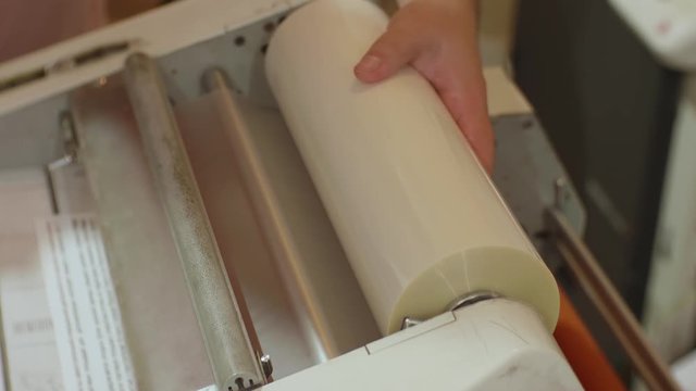 Hands of white man run a roll laminator during its work. Closeup view