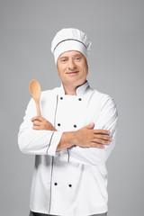 Male chef in uniform holding wooden spoon on grey background