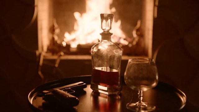 Crystal carafe with whiskey and the glass opposite the fireplace on eve. Pistol on the table