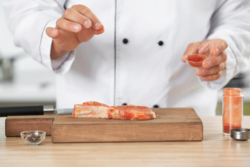 Male chef adding seasoning to meat in kitchen, closeup