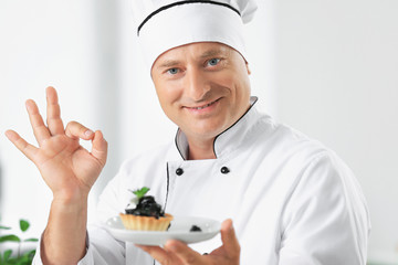 Male chef holding plate with dessert in kitchen