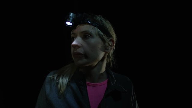 Endurance training group running in the woods at night, focus on woman who stops to get her breath back.
