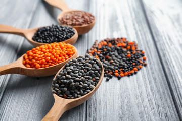 Spoons with different lentils on wooden background