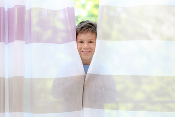 Cute little boy hiding behind curtains at home