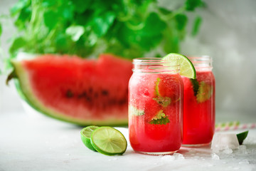 Fresh red watermelon slice and smoothie in glass jar with straw, ice, mint, lime on light background, copy space
