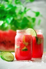 Fototapeta na wymiar Fresh red watermelon smoothie in glass jar with straw, ice, mint and lime on light background, copy space