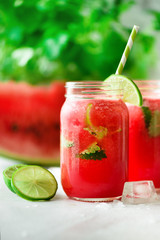 Fresh red watermelon smoothie in glass jar with straw, ice, mint and lime on light background, copy space