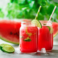 Fototapeta na wymiar Fresh red watermelon slice and smoothie in glass jar with straw, ice, mint, lime on light background, copy space
