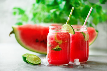Fresh red watermelon slice and smoothie in glass jar with straw, ice, mint, lime on light background, copy space