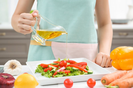 Woman pouring cooking oil onto vegetable salad in kitchen