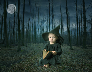 little halloween witch reading a magic book in a fairy tale forest
