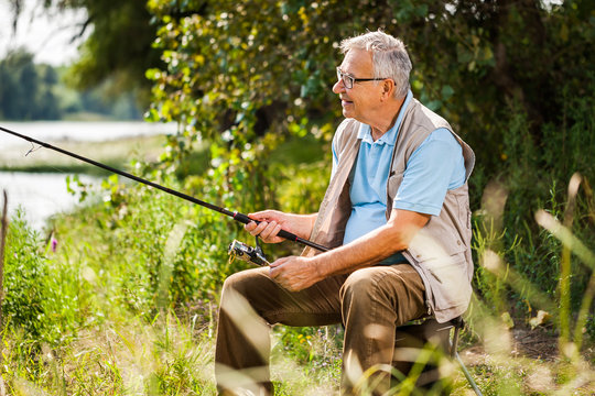 Happy senior man is fishing on sunny day. 