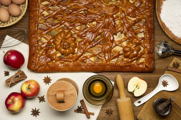 Apple pie with baking ingredients, spices and kitchen tools for cooking, rustic homemade sweet food on wooden table, top view 