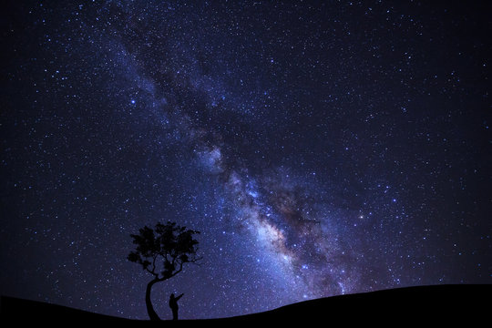 A Man is standing unter tree pointing on a bright star with milky way galaxy and space dust in the universe