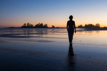 Beautiful woman in a nice casual dress is walking bare feet on a sandy beach during a vibrant summer sunset. Taken in Tofino, Vancouver Island, British Columbia, Canada.
