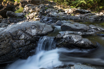 Fototapeta premium Water spring running down the smooth rocks in a beautiful canyon. Taken in Sooke Potholes Provincial Park near Victoria, Vancouver Island, BC, Canada. 