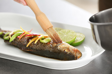 Chef covering fish in serving plate with tasty sauce, closeup