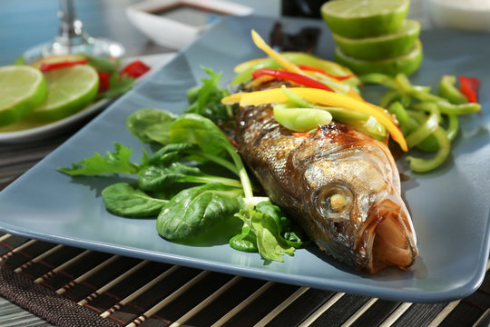 Serving plate with delicious fish in sauce and garnish on table, closeup