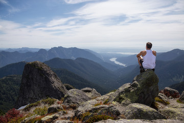 Fit and Adventurous Latin American man is hiking on top of a mountain ridge with a beautiful ocean view in the background. Taken at Lions Peaks, North of Vancouver, British Columbia, Canada.
