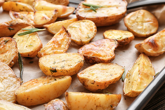 Delicious baked potatoes with rosemary on baking tray, closeup