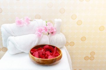 White towel rolls on top with pink flower and Thai Herbal Compress prepared on massage table for spa treatment