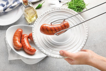 Woman putting grilled sausage on plate