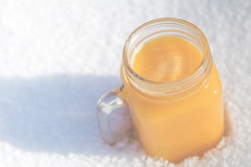 Winter vitamins immunity concept . Freshly squeezed Orange citrus juice for health in glass jar on snow.