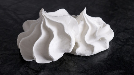 Sweet white meringue is isolated on a dark background.