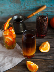 Layered non-alcoholic cocktail recipe idea. Orange juice in the bottom and dark coffee on the top in the glass. Bright and cozy still life of coffee beans, orange slices and layered cocktail.