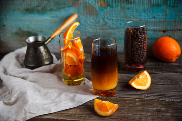 Layered non-alcoholic cocktail recipe idea. Orange juice in the bottom and dark coffee on the top in the glass. Bright and cozy still life of coffee beans, orange slices and layered cocktail.