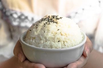 Female's hand holding a bowl with cooked rice,Jasmine rice background on hand.Hand of woman holding a white rice in the bowl.