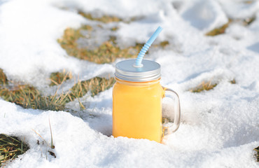 Winter vitamins immunity concept . Freshly squeezed Orange citrus juice for health in glass jar on snow.
