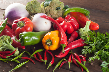 Harvest of different peppers and vegetables on a wooden background